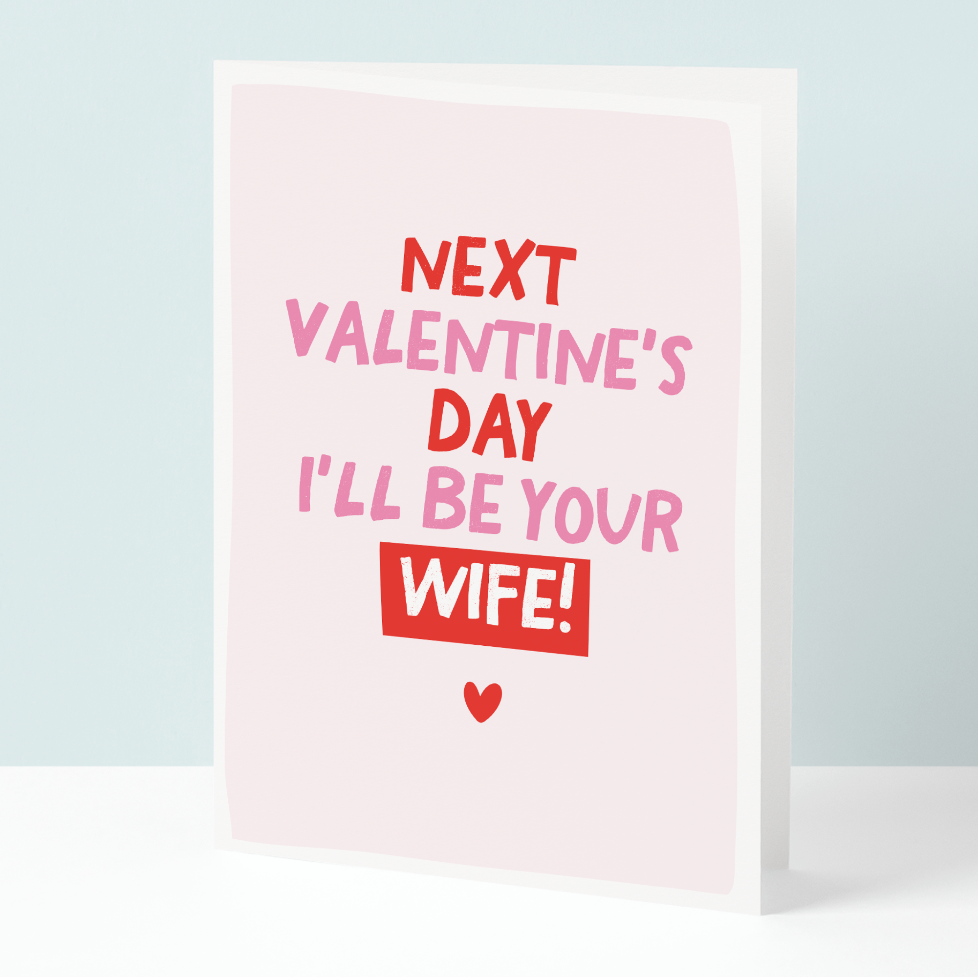 Valentine's Day card with text 'Next Valentine's Day I'll be your wife!' on a light pink background.